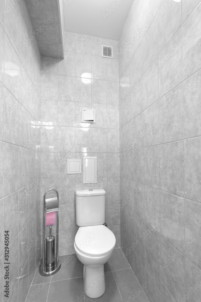 White toilet in the toilet room. Gray tiles on the walls in the toilet