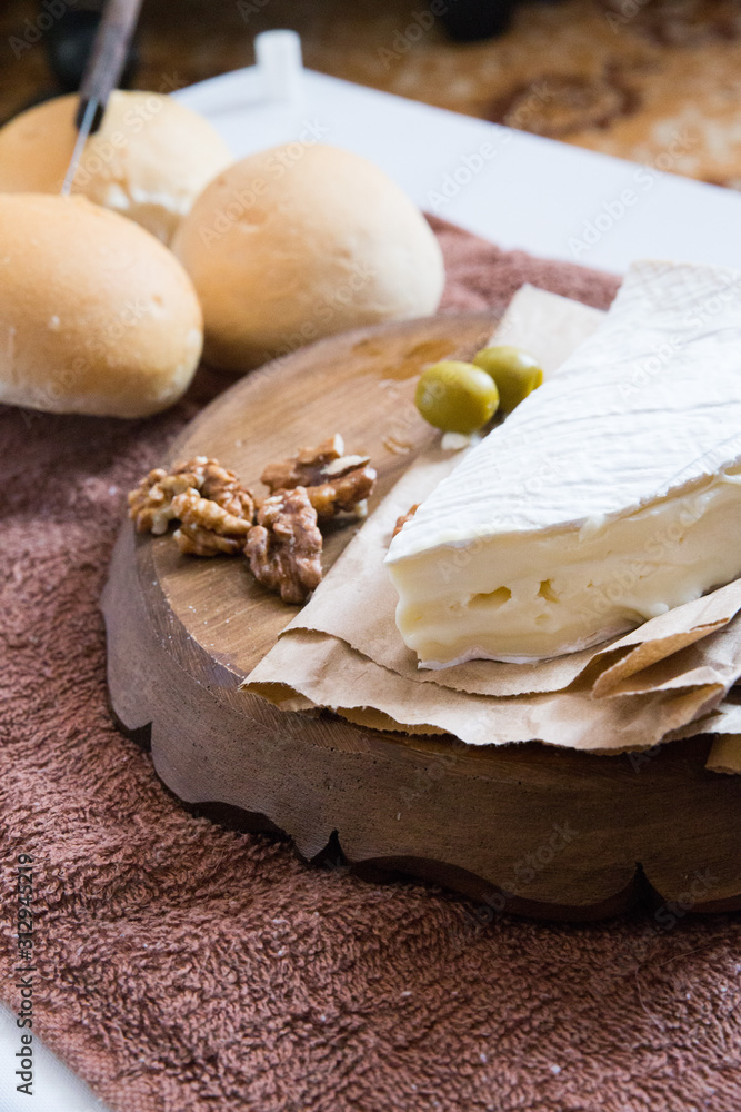 vertical photo, brie cheese next to lie nuts and olives on a wooden board next to fresh buns vertical photo, brie cheese next to lie nuts and olives on a wooden board next to fresh buns