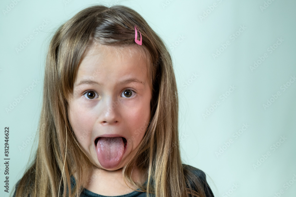 Close-up portrait of little girl with long hair sticking out her tongue. - obrazy, fototapety, plakaty 