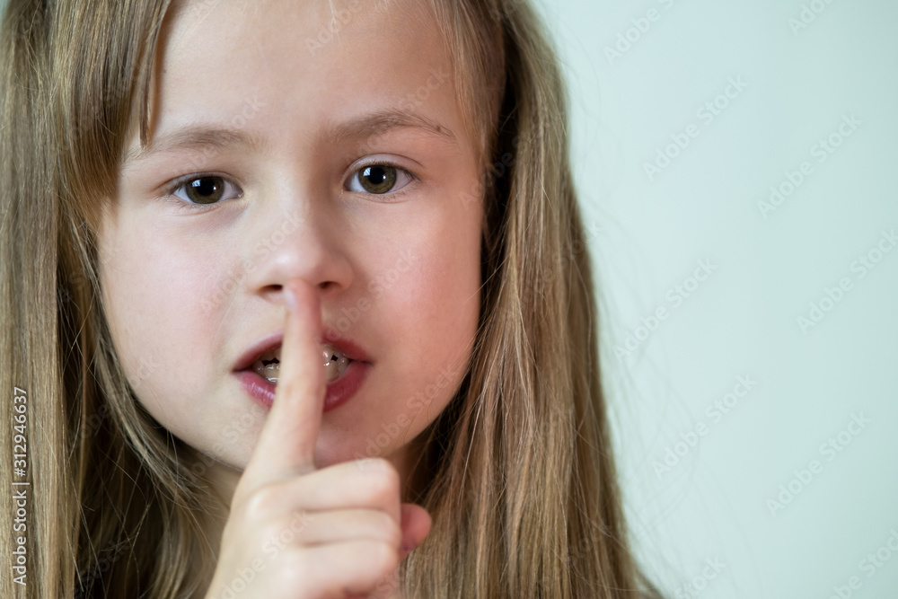Close-up portrait of little child girl with long hairholding point finger to her lips making hush gesture. Close-up portrait of little child girl with long hairholding point finger to her lips making hush gesture.