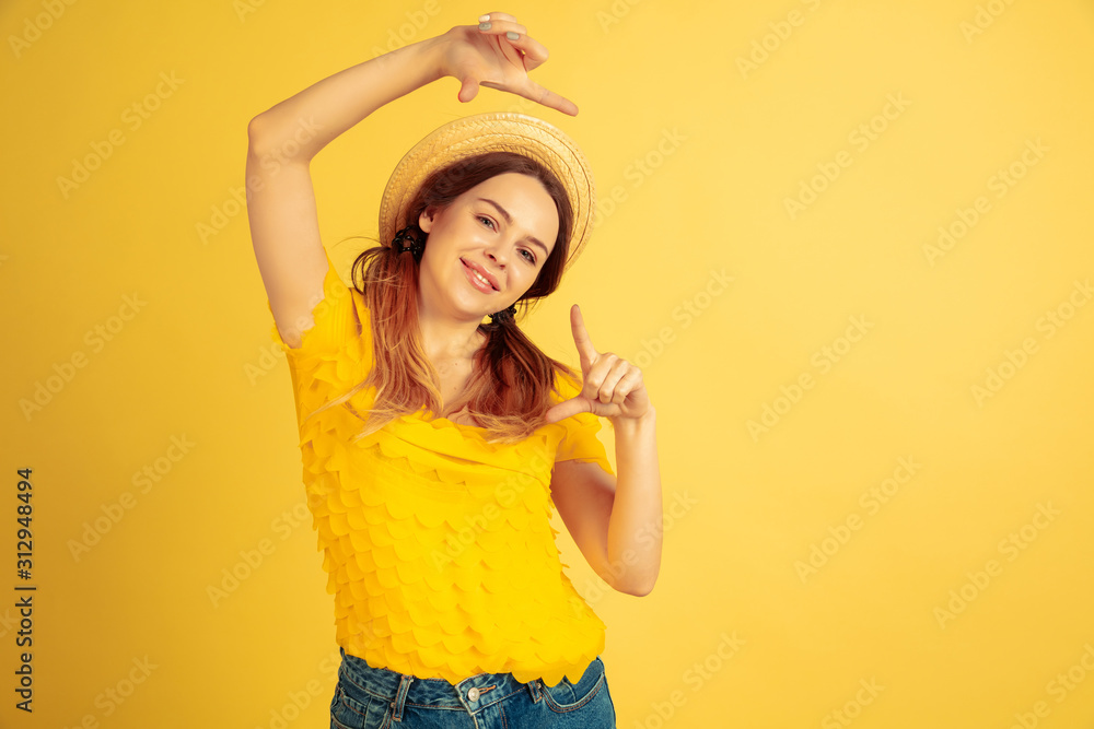 Framing, selfie, smiling. Caucasian woman's portrait on yellow studio background. Beautiful female model in hat. Concept of human emotions, facial expression, sales, ad. Summertime, travel, resort. Framing, selfie, smiling. Caucasian woman's portrait on yellow studio background. Beautiful female model in hat. Concept of human emotions, facial expression, sales, ad. Summertime, travel, resort.