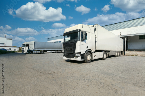 white truck with a white trailer at unloading at the warehouse.Warehouse complex with an asphalt pad and truck with blue sky
