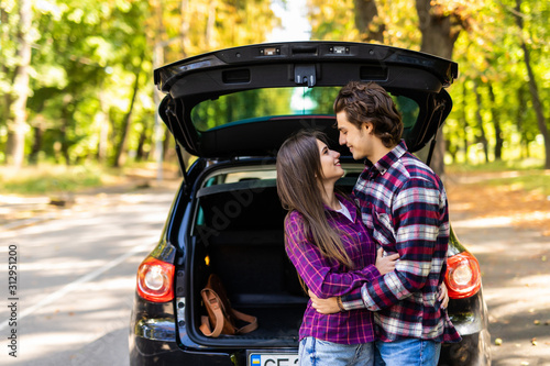 Beautiful carefree couple discovering the world traveling by car. Young man and woman hugging and touching each other while sitting in the car trunk © F8  \ Suport Ukraine