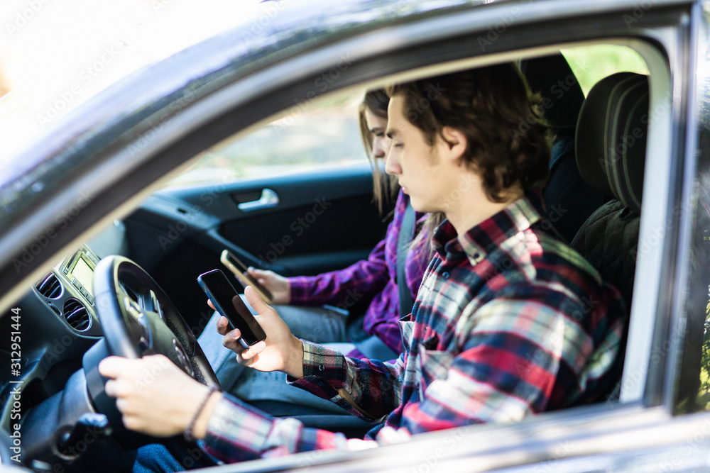 Portrait of a young couple texting while driving together on the road