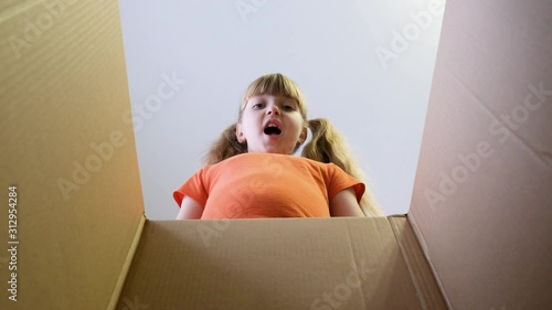 The child opened a box with a gift. A little girl looks in the box, is surprised and happy to receive a surprise. Slow Motion.