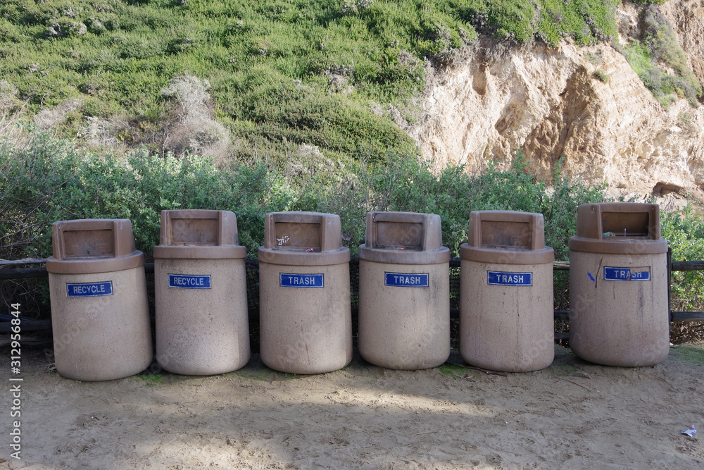 A battery of recycling and trash cans lined up at a public beach park A battery of recycling and trash cans lined up at a public beach park