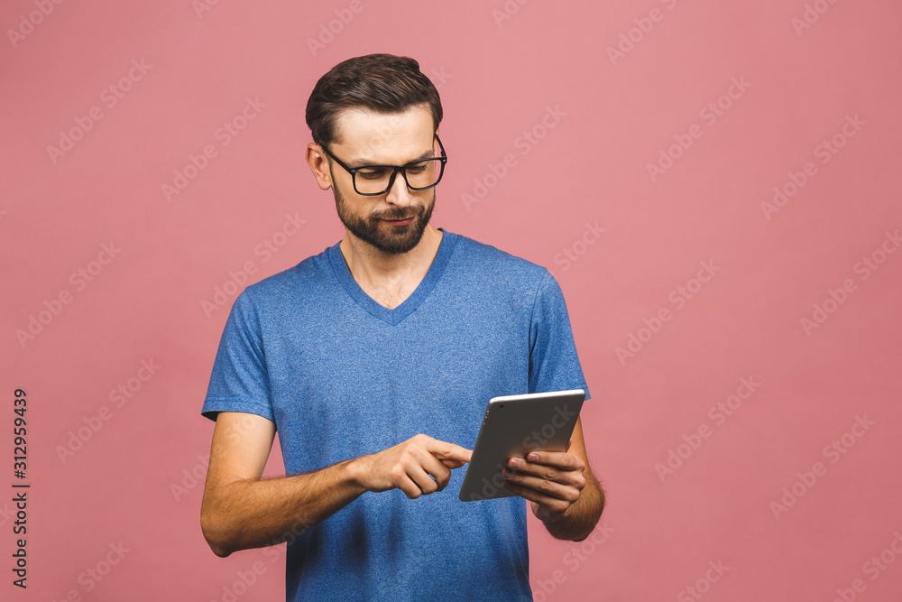 Happy young man in casual standing and using tablet over pink background Happy young man in casual standing and using tablet over pink background