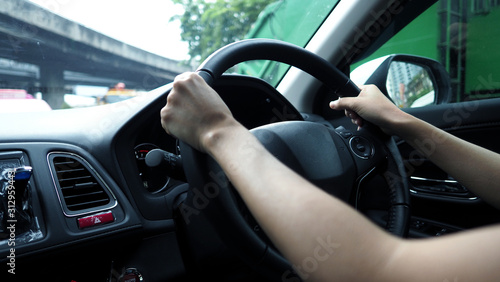 Close-up images of woman hands driving and controling car with confidence and safety which car moving to the Bangkok city Thailand for roadtrip and on the road no traffic jam. © gnepphoto