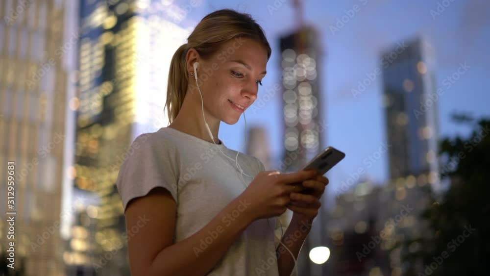 Beautiful woman using electronic headphones and smartphone internet connection for listening positive audio book, happy girl enjoying leisure time on urban setting Beautiful woman using electronic headphones and smartphone internet connection for listening positive audio book, happy girl enjoying leisure time on urban setting