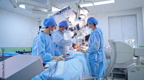 Group of surgeons performing operation to a patient. Doctors in medical uniform look into modern microscope during surgery in the operating room. photo
