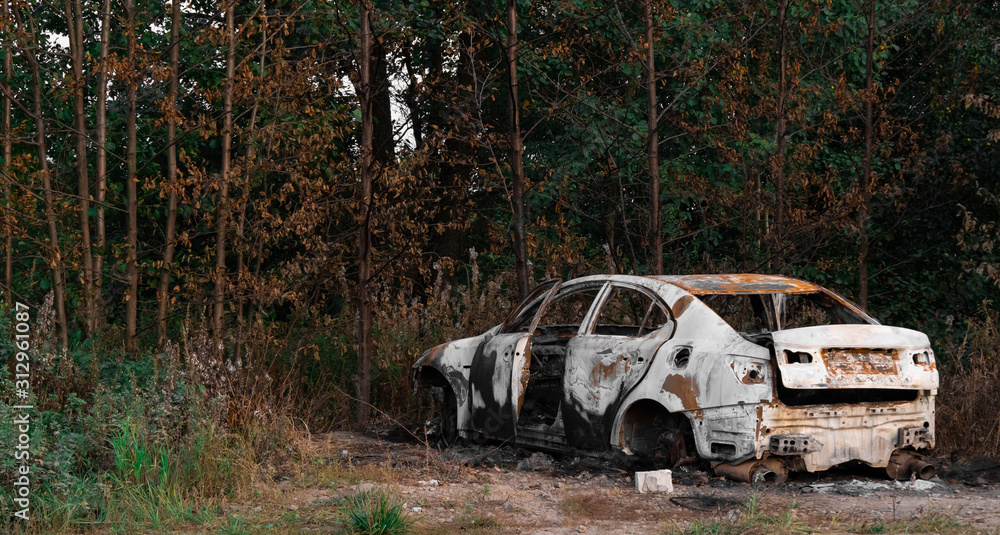Burnt out, Wrecked car after an explosion or fire. Rusty, burnt car interior with ash, molten glass and metal parts. Abandoned car in the forest near the city. The concept of a traffic accident.