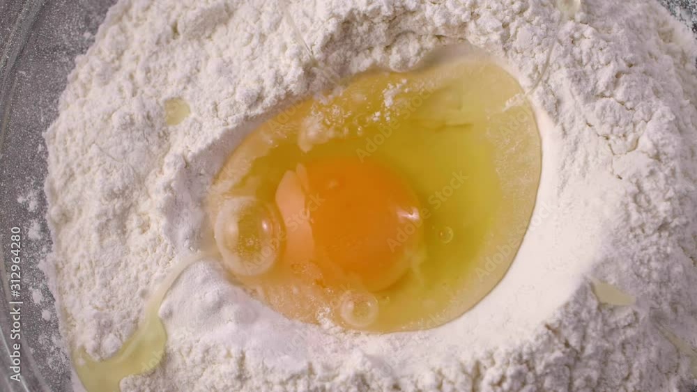 Slow motion of falling eggs into flour stock. Footage food. Egg dropping into flour, slow motion. Preparation of the dough.Closeup shot of male chef cracking egg in glass bowl with flour top view. Slow motion of falling eggs into flour stock. Footage food. Egg dropping into flour, slow motion. Preparation of the dough.Closeup shot of male chef cracking egg in glass bowl with flour top view.
