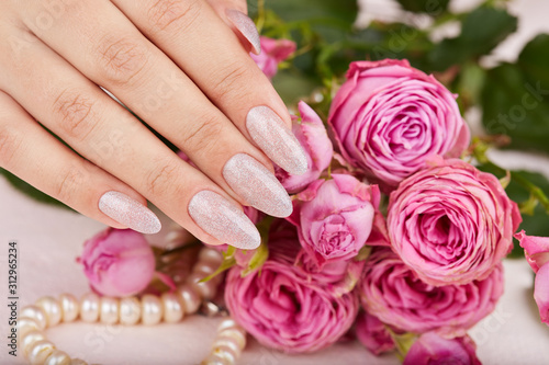Hand with long artificial manicured nails colored with nail polish with silver glitter and pink roses
