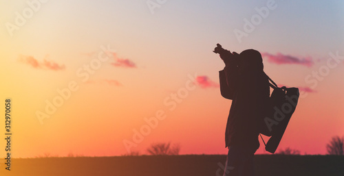 photographer with a tripod and camera takes a landscape during sunset in a large open area