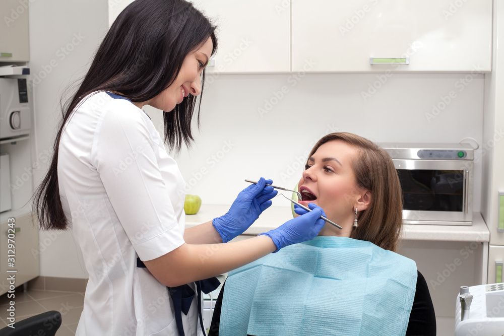 The dentist examines the patient's mouth, they smile and look into the frame, against the background of medical equipment with a green Apple in their hands. The concept of a healthy beautiful smile. The dentist examines the patient's mouth, they smile and look into the frame, against the background of medical equipment with a green Apple in their hands. The concept of a healthy beautiful smile.