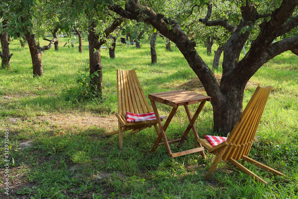 Wooden chairs and table under tree in a beautiful garden Wooden chairs and table under tree in a beautiful garden