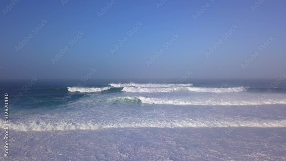 Aerial, drone shot over huge dangerous waves moving towards the coast of Portugal, on a misty and sunny morning, in the Lisbon District Aerial, drone shot over huge dangerous waves moving towards the coast of Portugal, on a misty and sunny morning, in the Lisbon District