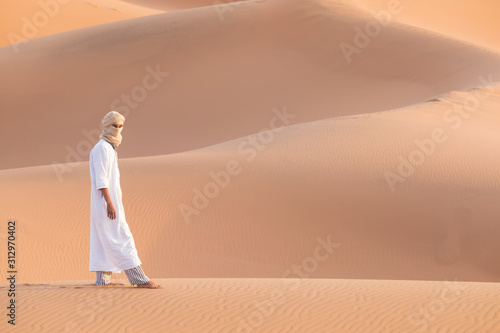 Bedouin on way through sandy desert. Beautiful sunset with big dunes on Sahara  Morocco. Silhouette nomad man. A touareg with his traditional clothes and turban. Picturesque background nature concept