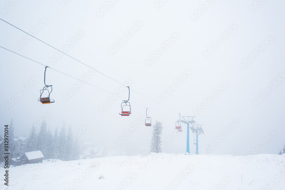 Scenic view of snowy mountain with gondola lift in fog Scenic view of snowy mountain with gondola lift in fog