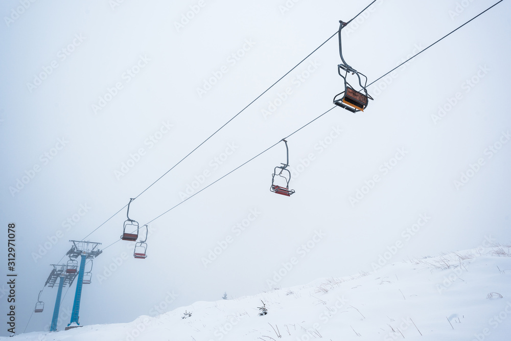 Scenic view of snowy mountain with gondola lift in fog Scenic view of snowy mountain with gondola lift in fog