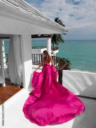 beautiful girl in a flying pink dress on the beach with sea view. dress flies in the wind