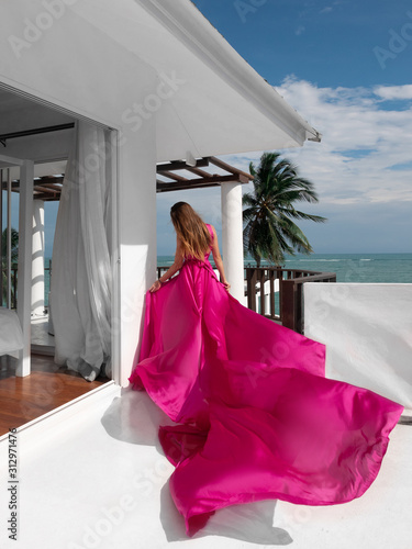 beautiful girl in a flying pink dress on the beach with sea view. dress flies in the wind
