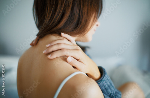 Close up of a brunette woman massing her neck in a bedroom
