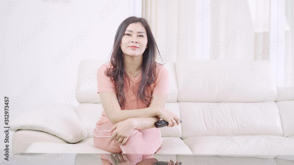 Pretty young woman watching TV while sitting on the sofa and holding the remote control in the living room at home. Shot in 4k resolution Pretty young woman watching TV while sitting on the sofa and holding the remote control in the living room at home. Shot in 4k resolution