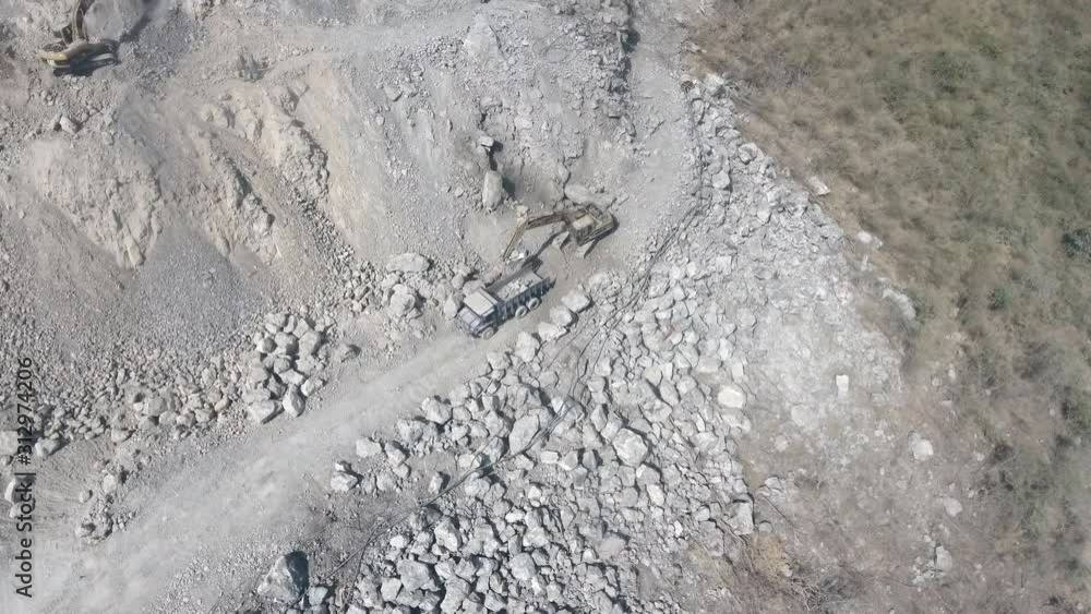 aerial drone shot : fly over an excavator loading rocks into a dump truck aerial drone shot : fly over an excavator loading rocks into a dump truck