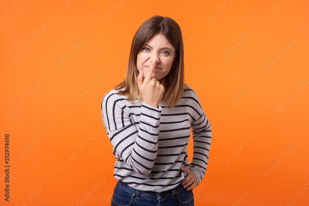 You are liar. Portrait of angry woman with brown hair in casual shirt standing with upset disappointed face and touching nose, showing lie gesture. indoor studio shot isolated on orange background You are liar. Portrait of angry woman with brown hair in casual shirt standing with upset disappointed face and touching nose, showing lie gesture. indoor studio shot isolated on orange background