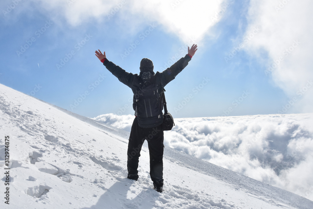 Happy mountaineer raise hand up on top of mountain. Climber enjoy on snowy mountain high above the clouds