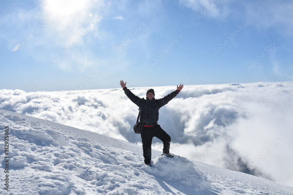 Happy mountaineer raise hand up on top of mountain. Climber enjoy on snowy mountain high above the clouds