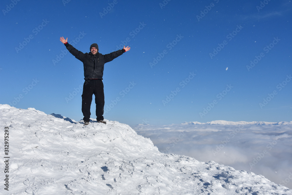 Happy mountaineer raise hand up on top of mountain. Climber enjoy on snowy mountain high above the clouds Happy mountaineer raise hand up on top of mountain. Climber enjoy on snowy mountain high above the clouds