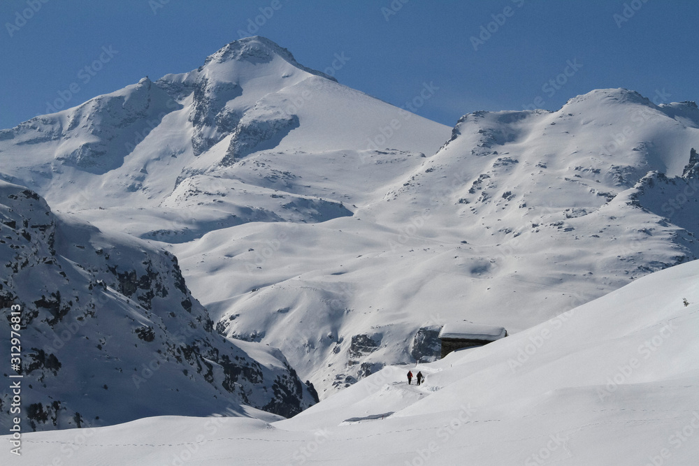 People walking toward cabin on remote, snow covered mountain, Vals, Canton of Grisons, Switzerland People walking toward cabin on remote, snow covered mountain, Vals, Canton of Grisons, Switzerland