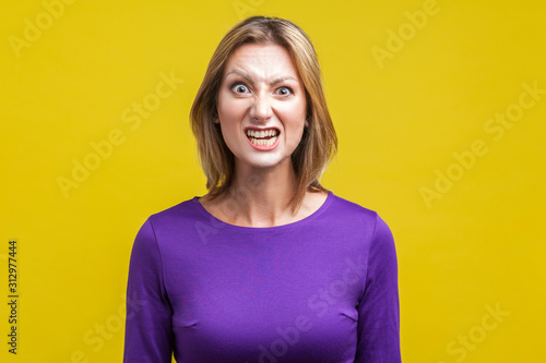 Papier peint Portrait of beautiful emotional woman in tight purple dress standing with clenched teeth and angry grimace on face, pretending to be aggressive