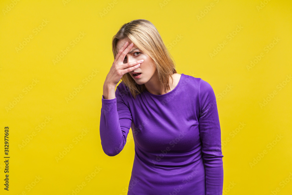 Portrait of curious young woman in elegant tight purple dress standing looking through fingers with prying eyes, spying with cunning face expression. indoor studio shot isolated on yellow background Portrait of curious young woman in elegant tight purple dress standing looking through fingers with prying eyes, spying with cunning face expression. indoor studio shot isolated on yellow background