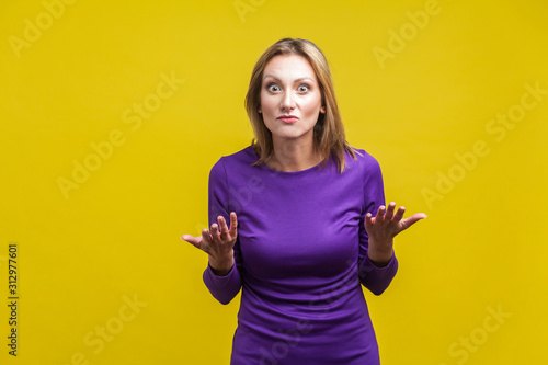 Fotografia How could you? Portrait of disappointed unhappy woman in elegant tight purple dress standing with raised hands asking what do you want, angry face