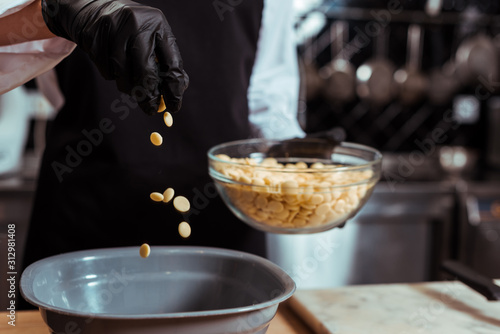 cropped view of chocolatier adding white chocolate chips into bowl in kitchen