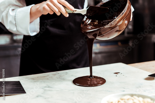 cropped view of chocolatier pouring melted chocolate on marble surface photo