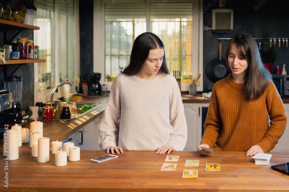 Two young femaies playing with tarot cards in a kitchen Two young femaies playing with tarot cards in a kitchen