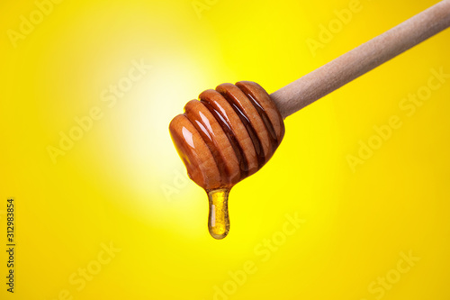 Dripping honey from dipper on yellow background, closeup