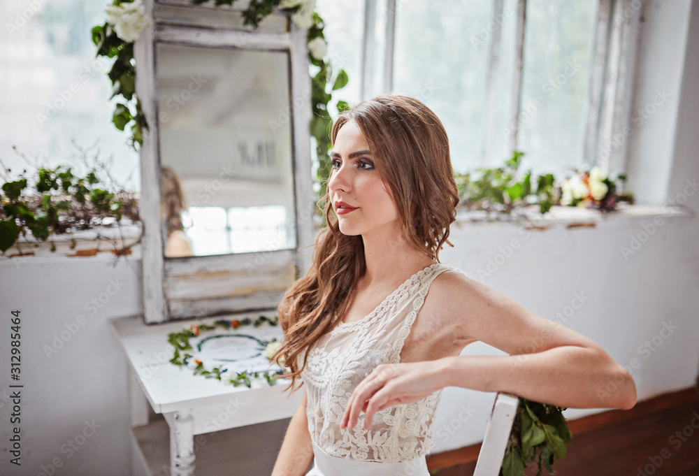 A beautiful bride in a white dress is sitting on a chair near the window and holding a wedding bouquet. A beautiful bride in a white dress is sitting on a chair near the window and holding a wedding bouquet.