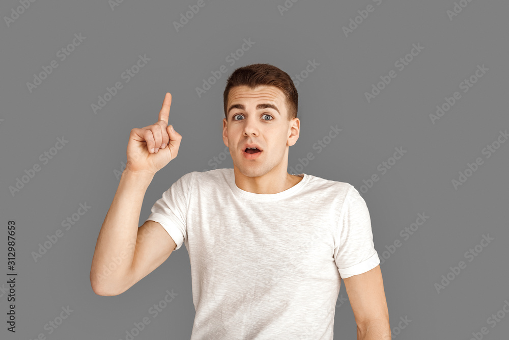Copy Space for Text or Product. Young man standing isolated on grey pointing up solution illuminated Copy Space for Text or Product. Young man standing isolated on grey pointing up solution illuminated