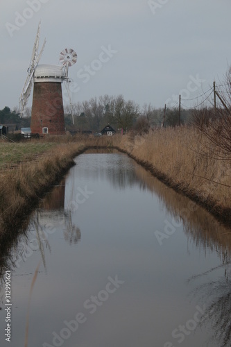 Beautiful rural landscape windmill brick building old brick vintage building Horsey Pump with wooden white sails on Norfolk Broad water canal flat en land East Anglia England cold pink sky reflected photo