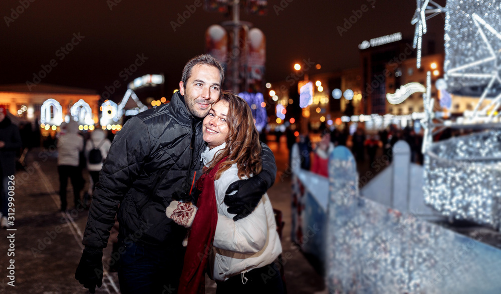 Loving couple walks around the evening Christmas city in winter.