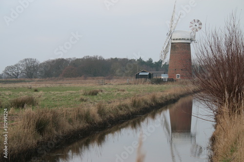 Beautiful rural landscape windmill brick building old brick vintage building Horsey Pump with wooden white sails on Norfolk Broad water canal flat en land East Anglia England cold pink sky reflected photo