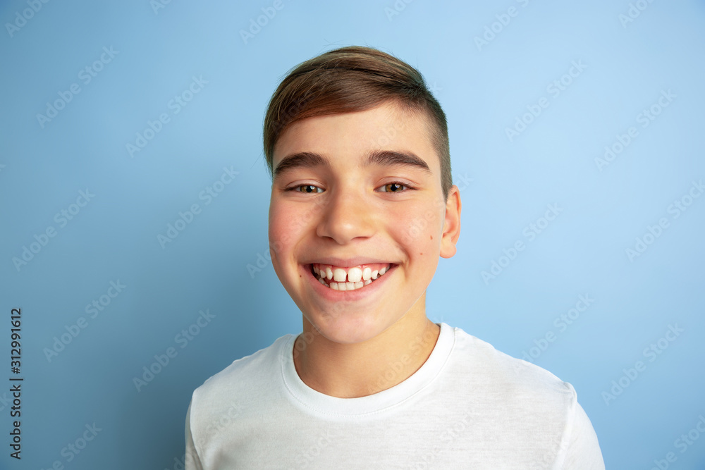 Smiling, happy. Close up. Caucasian boy portrait isolated on blue studio background. Beautiful teen male model in white shirt posing. Concept of human emotions, facial expression, sales, ad. Smiling, happy. Close up. Caucasian boy portrait isolated on blue studio background. Beautiful teen male model in white shirt posing. Concept of human emotions, facial expression, sales, ad.