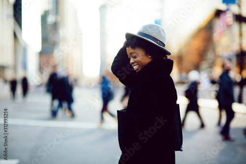Portrait of a happy smiling woman in faux fur coat and leather bag crossing a busy urban street