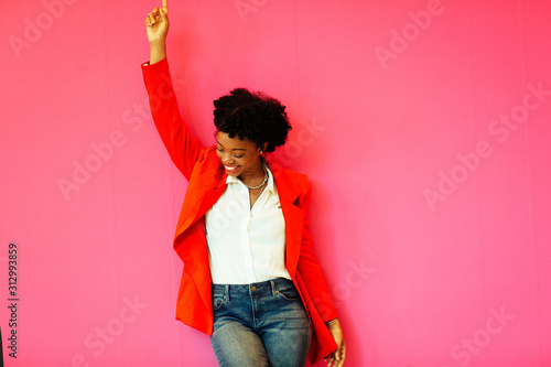 Portrait of a laughing young woman with arm up celebrating victory in front of a pink background photo