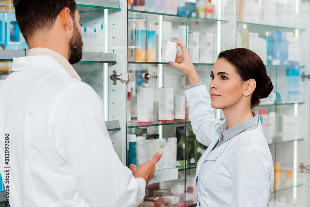 Pharmacists with jar of pills beside drugstore showcase